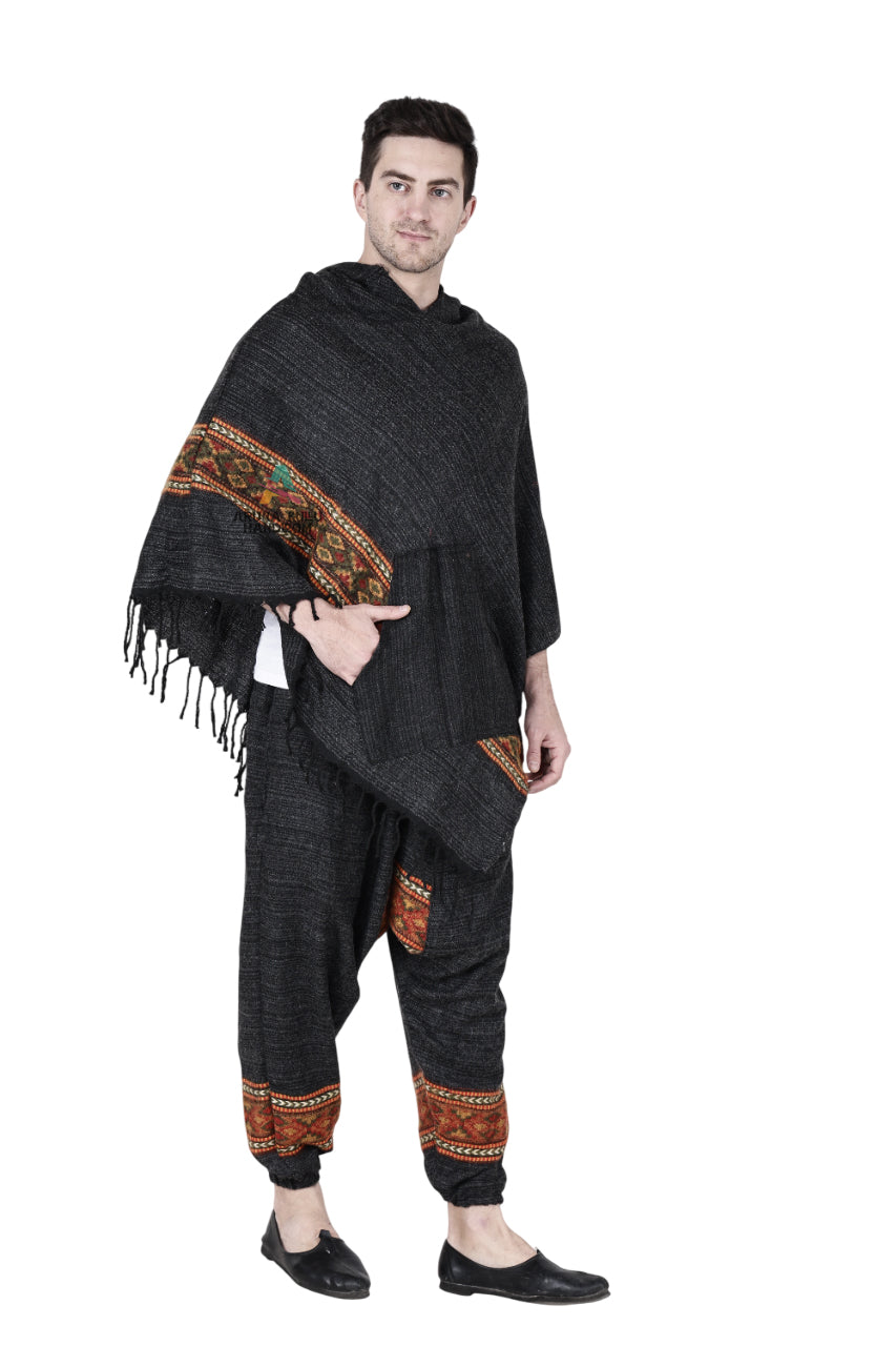 A man wears the Aruna Kullu Handloom Combo pajama and poncho black singal patti set, featuring a fringed, embroidered poncho and matching black pajama pants with decorative cuffs, paired with black slip-on shoes.