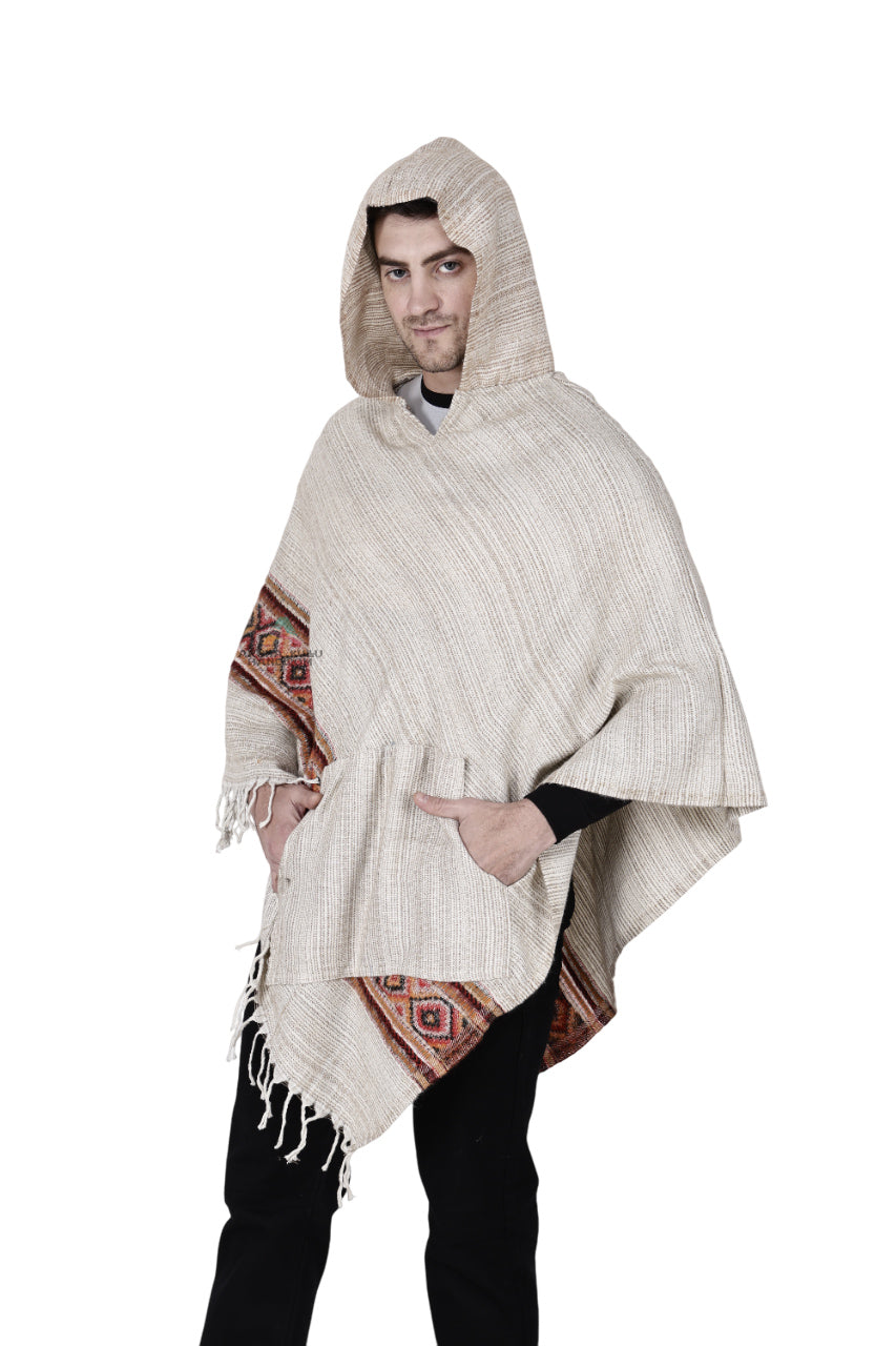 Someone wears a kullu shawl woolen poncho with hood in white, featuring decorative patterns and hand-woven embroidery, standing with hands in pockets against a white background.