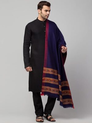 A man wears a black kurta and pants with a buttoned neckline, paired with the "Men shawl Kullu Wool lohi Genuine Hand Woven for Men 3 Patti blue" by aruna kullu handloom, featuring red and gold borders, against a plain grey background.