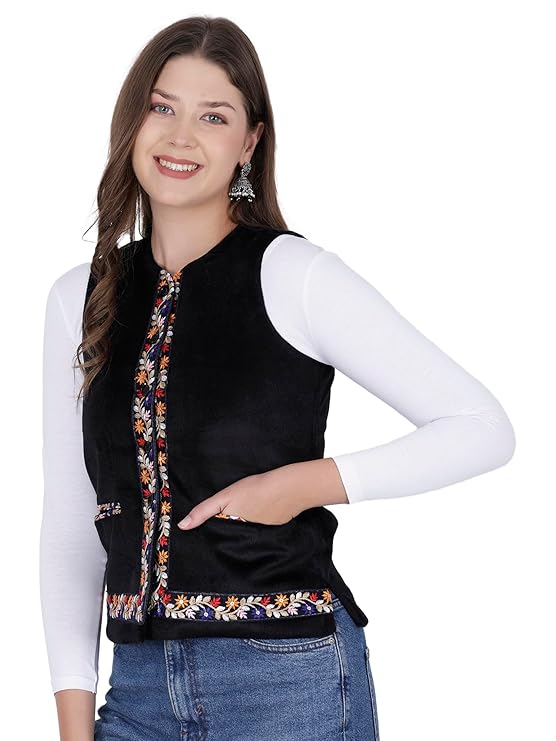 A smiling woman with long brown hair wears the aruna kullu handloom Nehru jacket for women with embroidery work in black over a white top and blue jeans, posing with one hand on her hip against a plain white background.