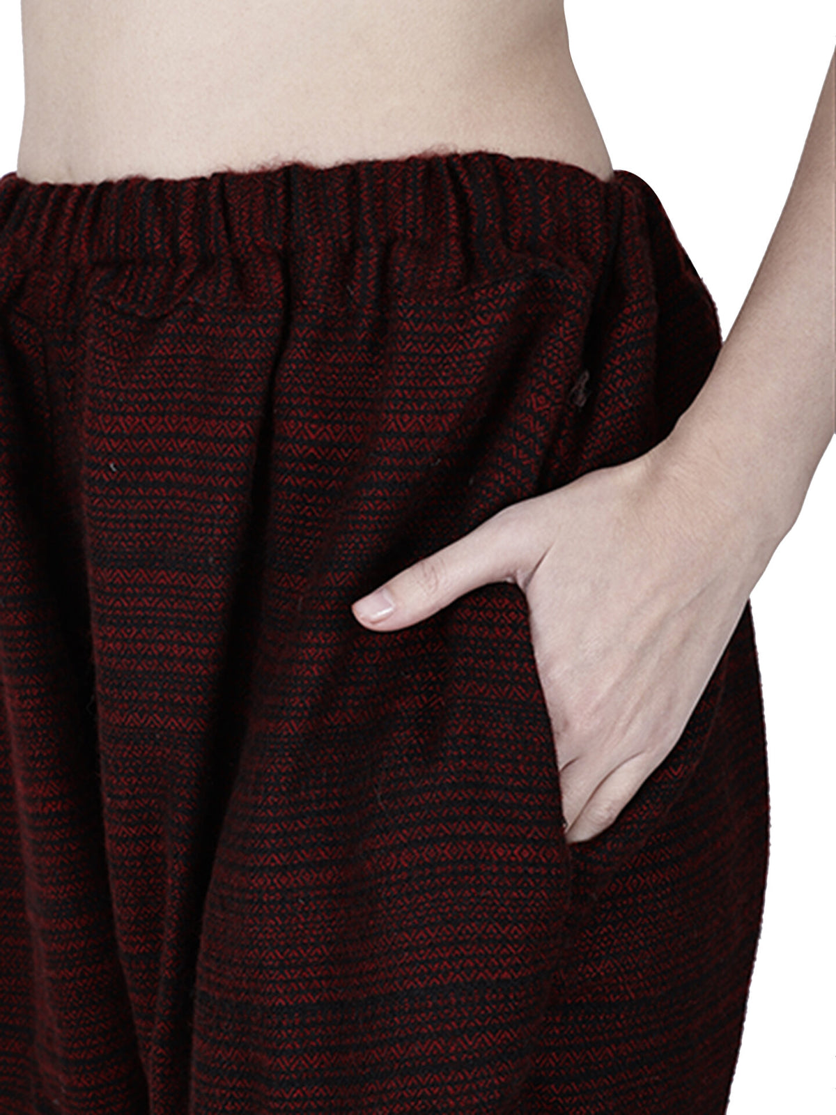A person wears loose yoga pajama maroon singal patti by aruna kullu handloom—dark red and black patterned woolen pants with elastic waistband, shown waist down against a white background, one hand in pocket. Ideal winter lower for men.