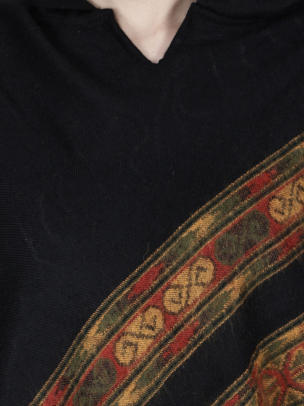 Close-up of a person wearing the Aruna kullu handloom shawl poncho for girls in black with 3 patti diagonal trim by aruna kullu handloom, showcasing decorative red, green, and gold patterns in a traditional Rajasthani style.