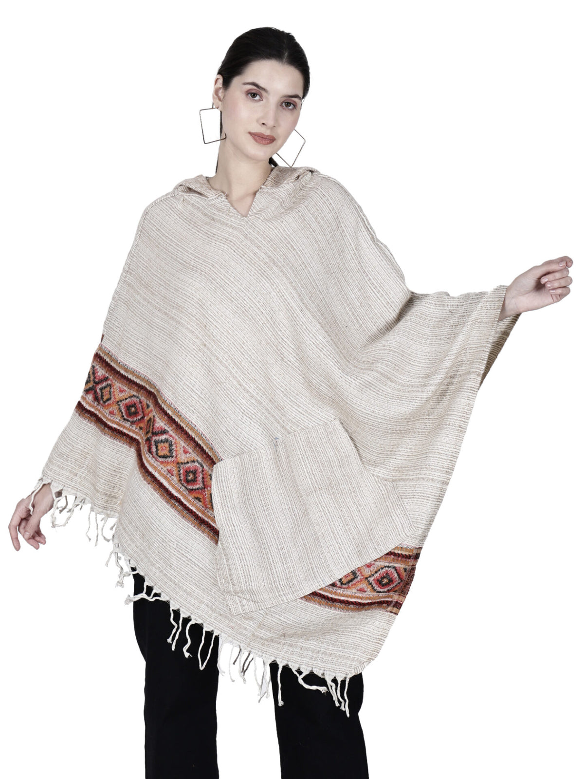 A woman models the Aruna Kullu Handloom cream woolen poncho with hood for ladies, styled with black pants, against a white background.
