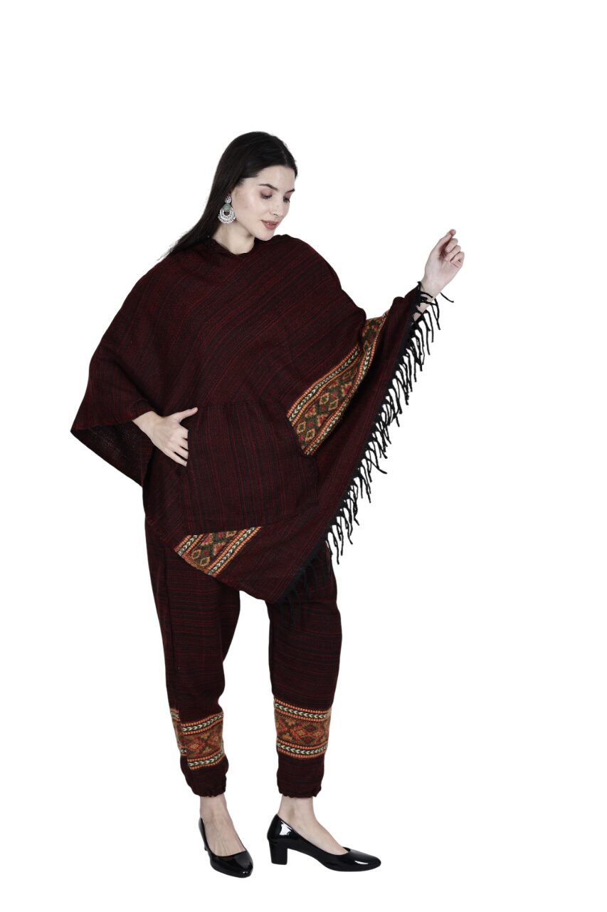 A woman models the aruna kullu handloom combo pajama and poncho singal patti maroon, showcasing its handwoven embroidery, patterned details, and fringes while posing against a white background.