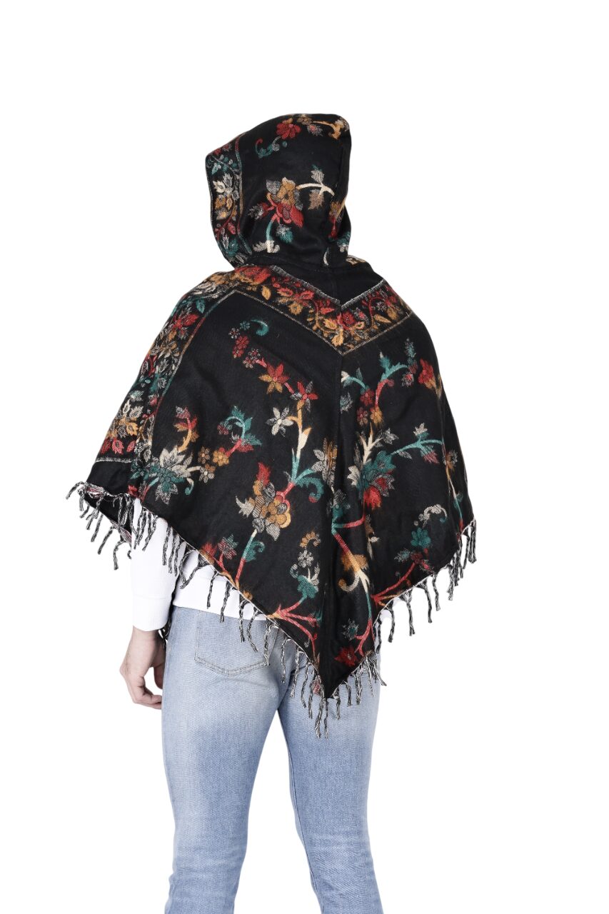 A person is seen from the back wearing the Kashmiri poncho black by aruna kullu handloom, featuring colorful floral patterns and tasseled edges, paired with light blue jeans and a white top against a white background.