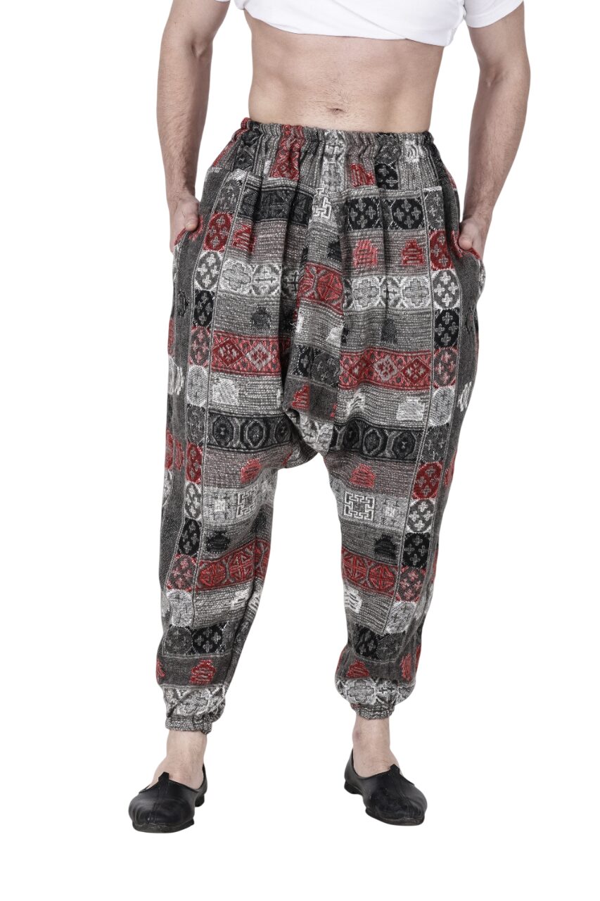 A person wearing aruna kullu handloom's Pajama for men loose yoga chess design with a red, black, and gray patchwork, hands in pockets, paired with black shoes and a cropped white shirt.