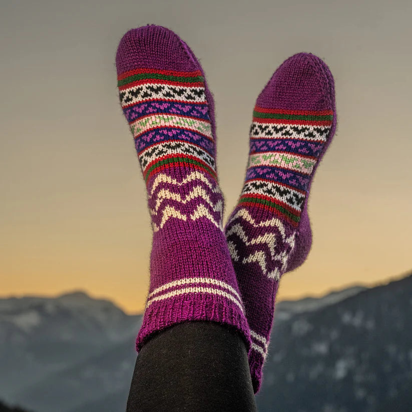 A person relaxes with their feet up, wearing aruna kullu handloom Woollen Traditional Hand Made Kullu Socks (Multicolour, Free Size), set against snowy mountains and a glowing sunset sky.