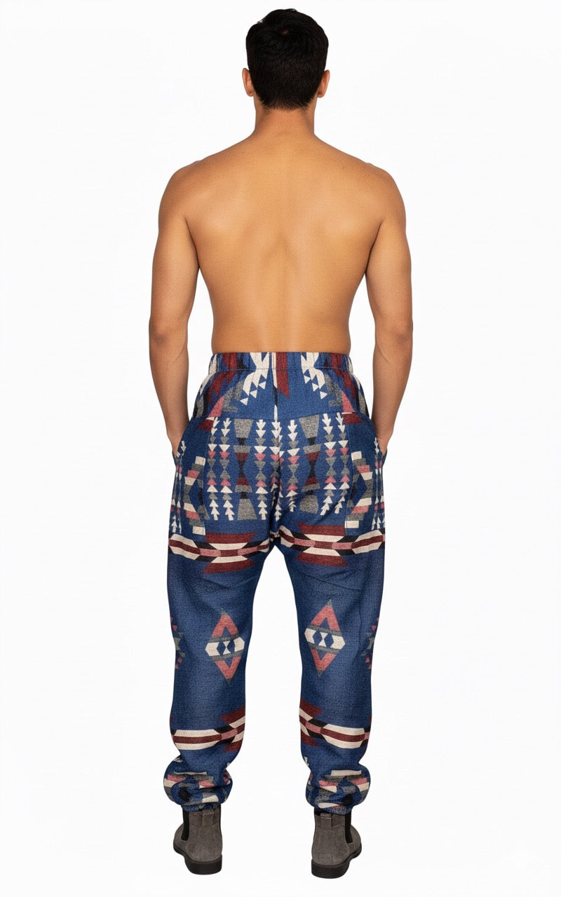 A shirtless man faces away, wearing aruna kullu handloom Wool Super Soft Warm Pajamas WITH KULLU PATTI WORK in blue, featuring bold geometric and tribal-inspired patterns in white, red, and beige. He also wears gray shoes against a plain white background.
