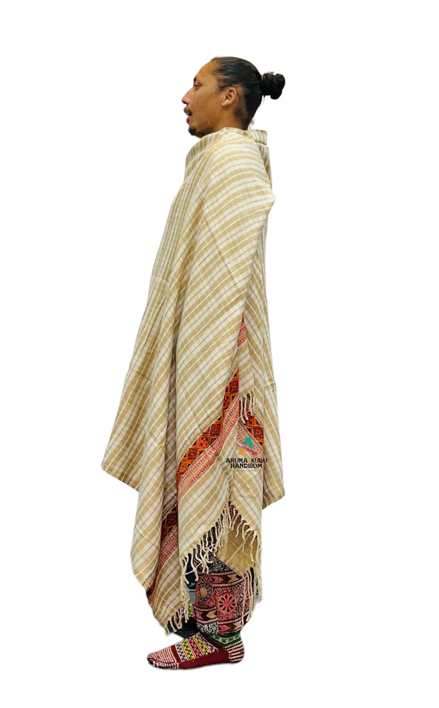 A person stands in profile wearing the ARUNA Genuine Hand Woven Kullu Wool LOI Men Shawl in cream with check and Kullu patti work by aruna kullu handloom, embroidered pants, and patterned shoes. Their hair is in a bun, mouth open against a white background.