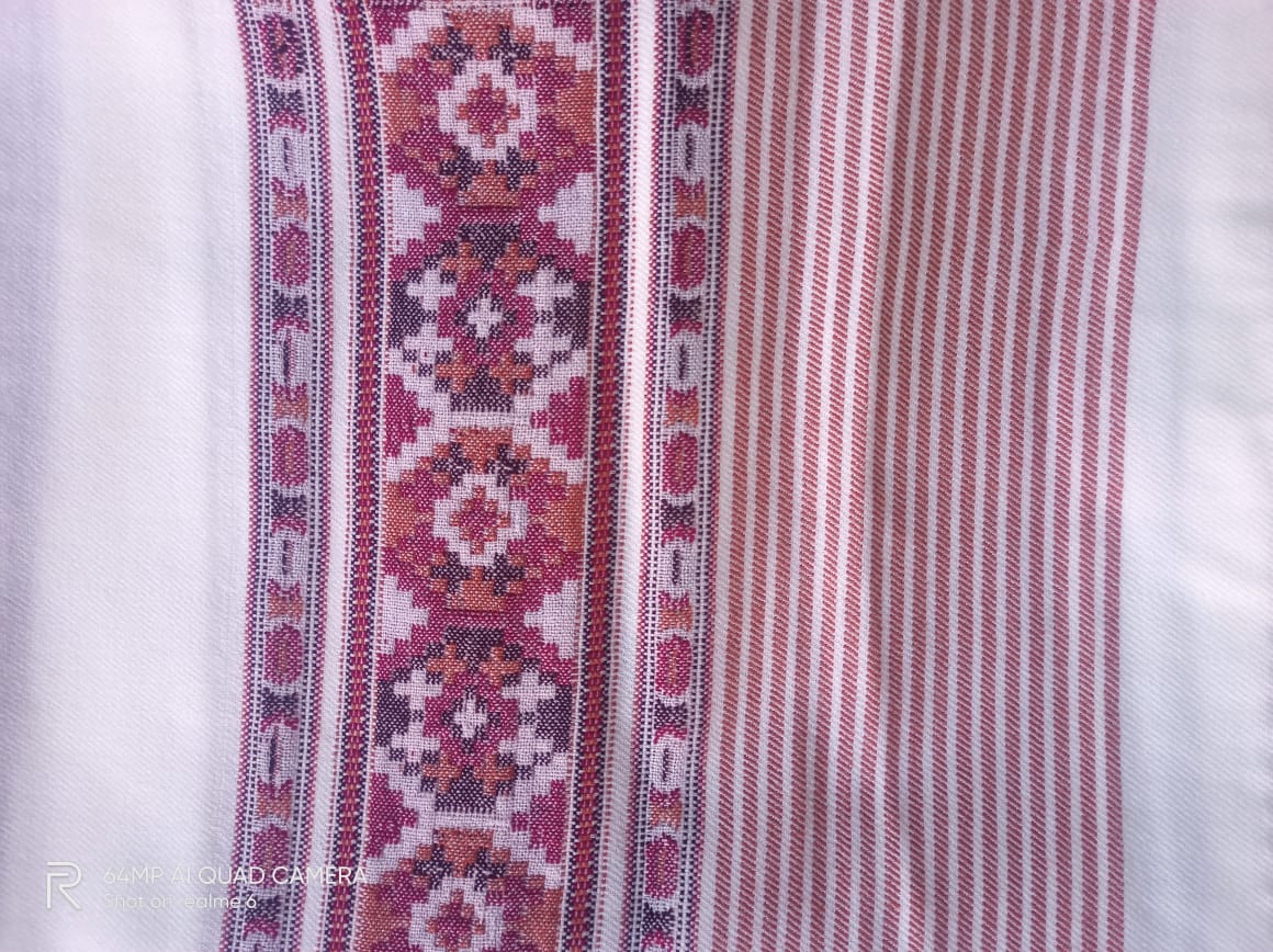 A close-up of the Hand Woven PASHMINA WHITE Shawl by aruna kullu handloom, featuring beautiful hand embroidery with traditional geometric patterns in red, white, and orange, plus red and white vertical stripes.