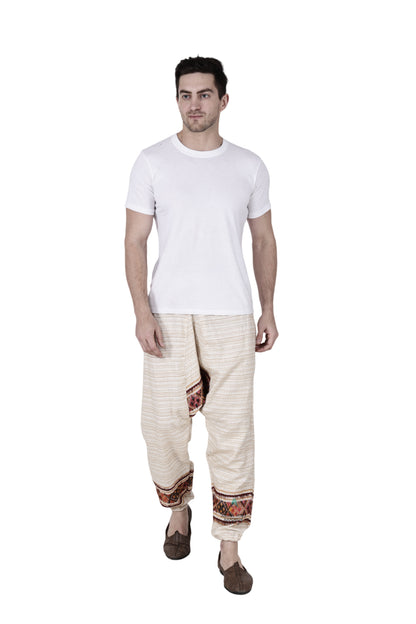 A man stands against a white background wearing an Aruna Kullu Handloom yoga pajama for men, loose single patti white, paired with a plain white T-shirt and brown sandals.