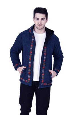 A man wears the aruna kullu handloom Kullu hoodie jacket for MEN in blue, featuring colorful kullu patti trim, over a white t-shirt and black pants. He stands facing forward with his hands in the jacket pockets, looking at the camera neutrally.