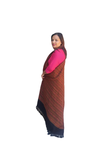 A woman with long dark hair stands sideways in a bright pink top, wearing an aruna kullu handloom Hand Woven PASHMINA black Shawl with beautiful embroidery over dark pants, against a plain white background.