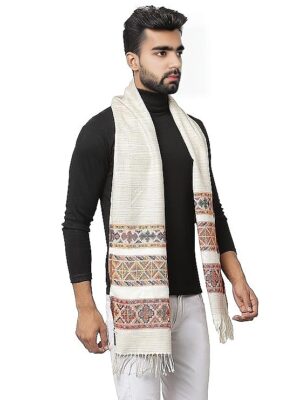 A man in a black turtleneck and white pants wears the "warm muffler Woollen Hand Woven Pure Embroidered white 3 patti" by aruna kullu handloom, a cream woolen muffler with multicolored patterns and fringed edges draped around his neck.