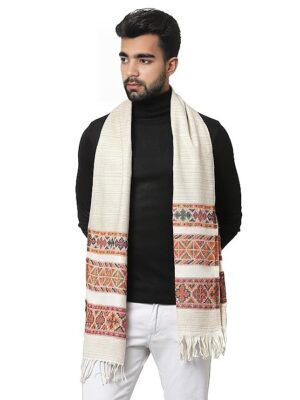 A man in a black turtleneck and white pants stands with the aruna kullu handloom warm muffler Woollen Hand Woven Pure Embroidered white 3 patti, featuring colorful patterns and fringed ends, draped around his neck.