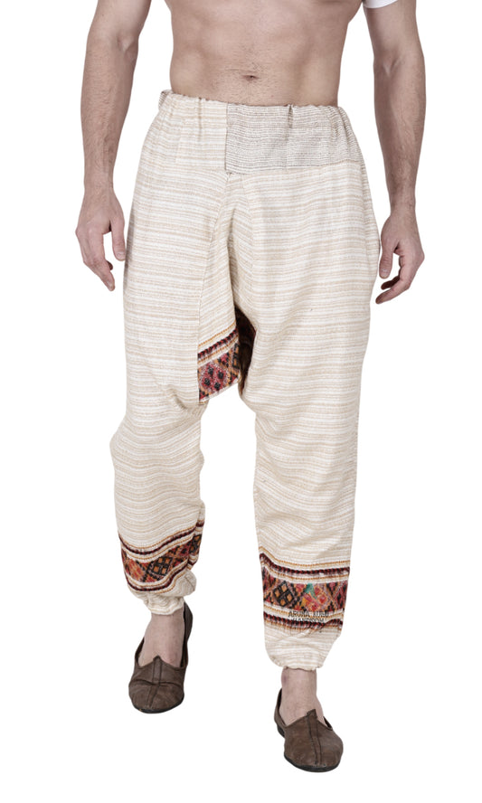 A person wears an Aruna Kullu Handloom yoga pajama for men, loose single patti in white, featuring decorative patterns near the ankles. The upper body is bare, arms relaxed at the sides, and paired with brown slip-on shoes.