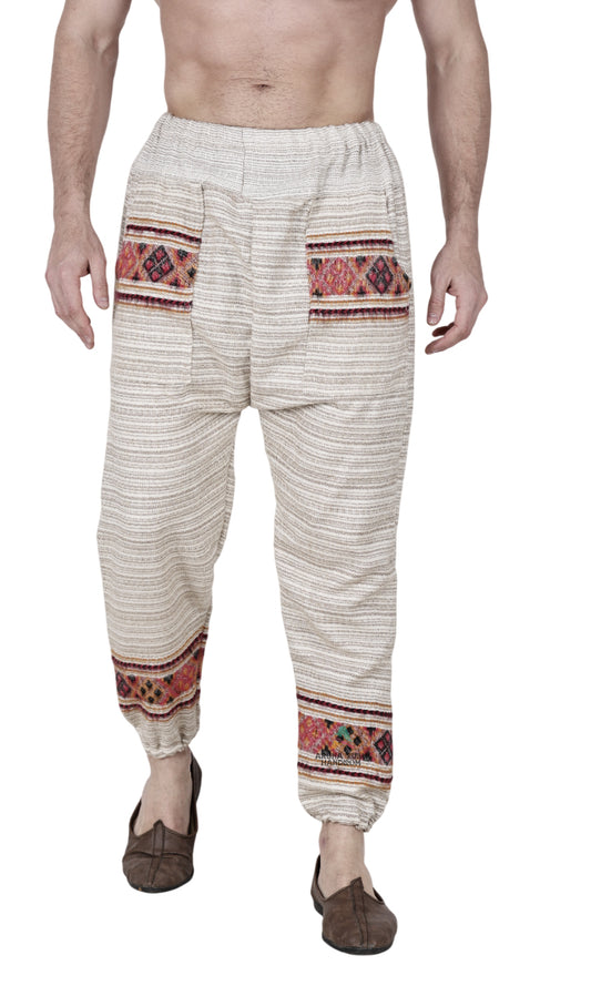 A person wears aruna kullu handloom's "Pajama for men white singal patti," featuring cream wool, colorful patterned bands with handwoven embroidery near pockets and lower legs, paired with brown shoes. Cropped at chest and ankles.