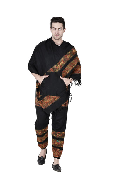 A person stands against a white background wearing the aruna kullu handloom Combo pajama and poncho black 3 patti, featuring colorful patterned bands on both pieces, fringe on the poncho edge, and their hands in the pockets.