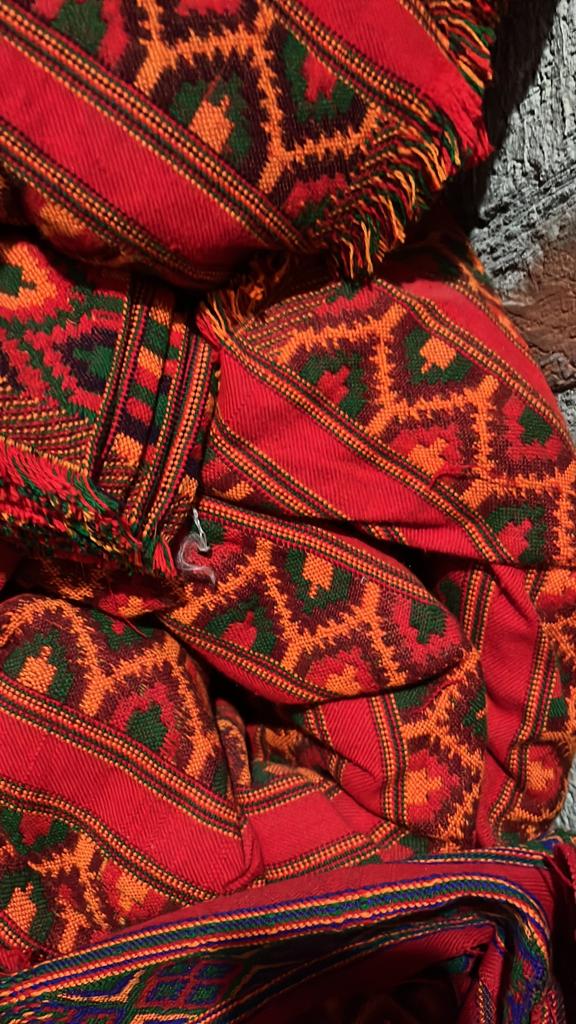 Close-up of aruna kullu handloom's KULLU Patti (LACE) Border for Suits, Kurtis, and Dress Material (3 M), showcasing vibrant red, green, orange, and black geometric patterns with traditional kullu border on a textured stone background.