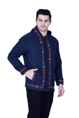 A man wears the aruna kullu handloom Kullu hoodie jacket for MEN in blue, featuring a colorful kullu patti trim, standing against a white background with one hand in his pocket.