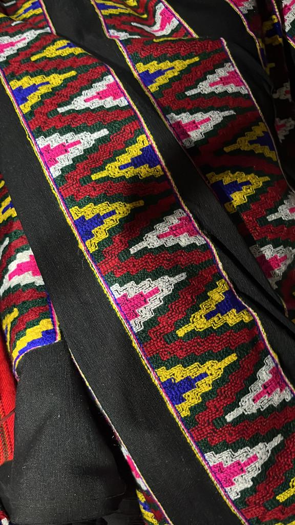 Close-up of aruna kullu handloom's KULLU Patti (LACE) Border for Suits, Kurtis, and Dress Material (3 M), featuring colorful traditional woolen fabric with intricate red, yellow, green, pink, blue & white geometric patterns and a black kullu border.