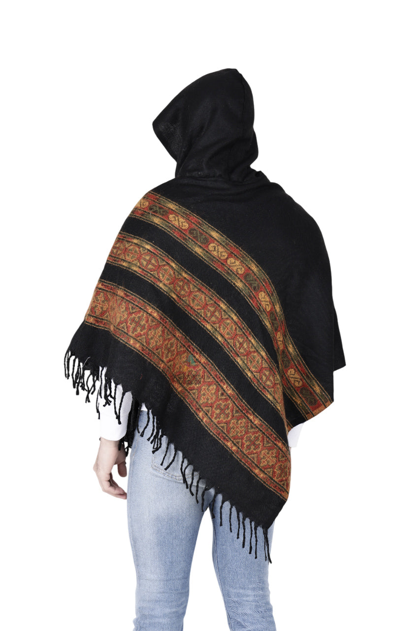A person wearing light blue jeans and the aruna kullu handloom "kullu shawl woolen poncho with hood black teen patti" stands facing away from the camera against a white background.