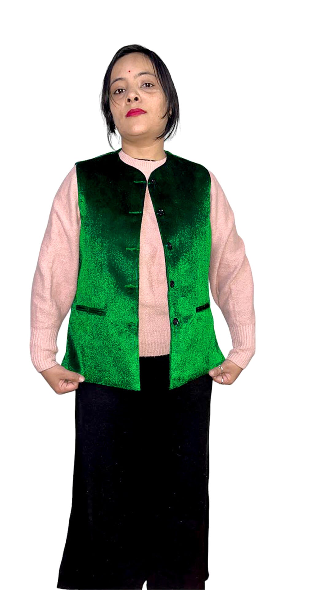 A woman with short dark hair and a red bindi poses facing forward, wearing an aruna kullu handloom Rampuri Kullu Nehru jacket for women in green, over a light pink sweater and long black skirt, holding the sides of her vest.