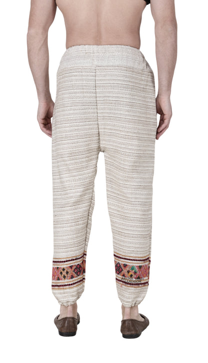 A person stands barefoot, facing away, wearing aruna kullu handloom's Pajama for men white singal patti with colorful patterned bands near the ankles and an elastic waistband. The background is white.