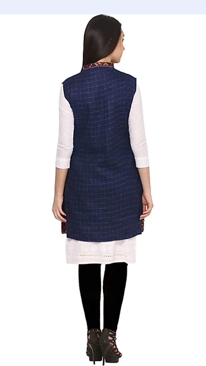 A woman with loose straight dark hair faces away from the camera, wearing aruna kullu handloom's Check navy blue long jacket with kullu lace work over a white kurta, black leggings, and heeled sandals.half jacket for women khadi half jacket for ladies ladies half jacket cotton women's half jacket ladies sadri design winter half jacket for women