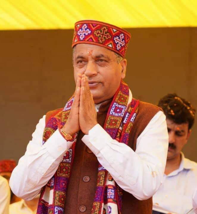 kinnauri muffler online men woolen muffler Himachal muffler online Himachal muffler kinnauri muffler A man wearing a traditional Himachali cap and an aruna kullu handloom Pure wool original Kullu Kinnauri muffler in white folds his hands in greeting against a yellow background.