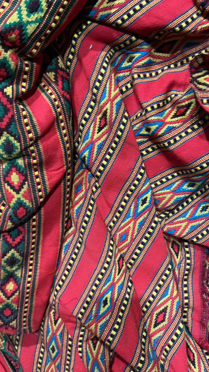 A close-up of aruna kullu handloom's vibrant red KULLU Patti (LACE) Border (3 M) for suits, kurtis, and dress material, featuring intricate geometric patterns in yellow, blue, green, and black with a traditional diamond and stripe design.