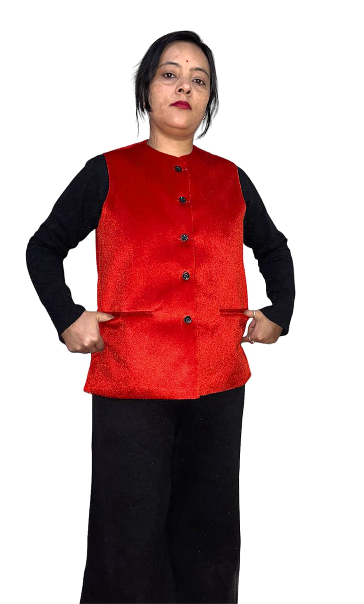 A woman stands with her hands in the pockets of an aruna kullu handloom Nehru jacket for women in red color, layered over a long-sleeved black top and black pants, against a plain white background.