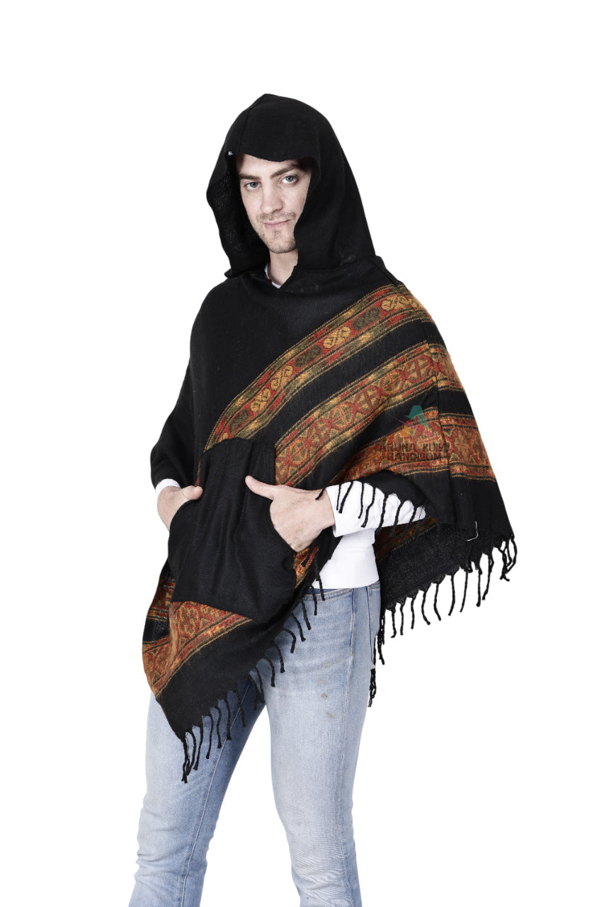 A person wears the aruna kullu handloom kullu shawl woolen poncho with hood black teen patti, featuring red and gold patterned stripes, paired with light blue jeans and a white shirt against a white background.
