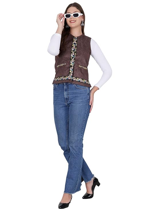 A woman in a white long-sleeve top, aruna kullu handloom Nehru jacket women with embroidery work (coffee), blue jeans, black heels, and white sunglasses poses confidently with one hand touching her sunglasses.