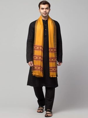 A man stands against a plain background wearing a black kurta pajama set, paired with the "aruna kullu handloom" Men shawl Kullu Wool lohi Genuine Hand Woven for Men 3 Patti in mustard, draped over his shoulders. He is also wearing black sandals.