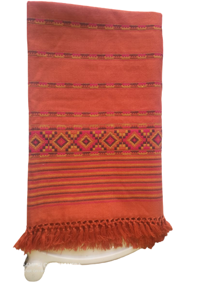 The aruna kullu handloom Hand Woven PASHMINA RUST COLOR Shawl for women features beautiful embroidery, a rich rust hue, and fringed edges, elegantly draped over a white surface.