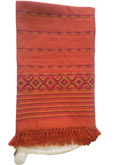 The aruna kullu handloom Hand Woven PASHMINA RUST COLOR Shawl for women features beautiful embroidery, a rich rust hue, and fringed edges, elegantly draped over a white surface.