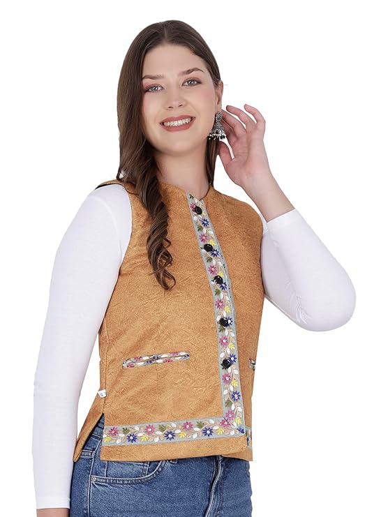 A smiling woman in an aruna kullu handloom Nehru jacket for women with embroidery work in yellow, over a white long-sleeve shirt and blue jeans, touches her earring while standing against a plain white background.