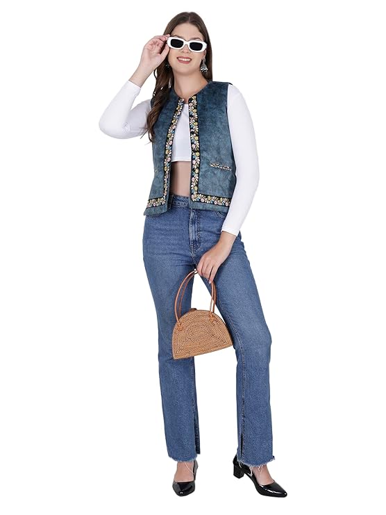 dhatu sadri for ladies A woman wearing white sunglasses, a white long-sleeve top, blue jeans, black shoes, and holding a brown handbag smiles against a white background, styled in the aruna kullu handloom Nehru jacket women with embroidery work blue.