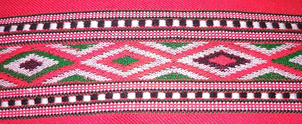 A close-up of aruna kullu handloom KULLU Patti (LACE) Border for Suits, Kurtis, and Dress Material (3 M), showcasing colorful woolen geometric patterns with diamond shapes and striped borders on a vibrant pink background.