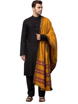 A man wearing a black kurta pajama and sandals stands holding the aruna kullu handloom Men shawl Kullu Wool lohi Genuine Hand Woven for Men 3 Patti mustard, showcasing exquisite Himalayan craftsmanship draped elegantly over his shoulder.