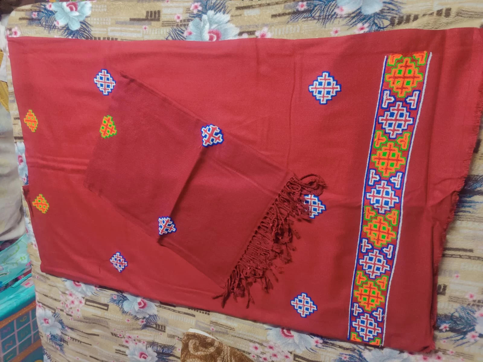 The aruna kullu handloom kullu patti woolen suit, 4 meters with stole in maroon, features colorful geometric embroidery and a multicolored border. One piece has fringed edges. Perfect for those seeking authentic Kullu suits online.