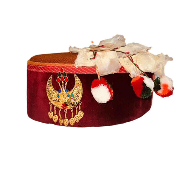 A Himachali topi in red velvet featuring golden flower embroidery and a Kalgi, decorated with colorful pom-poms, displayed on a white background.