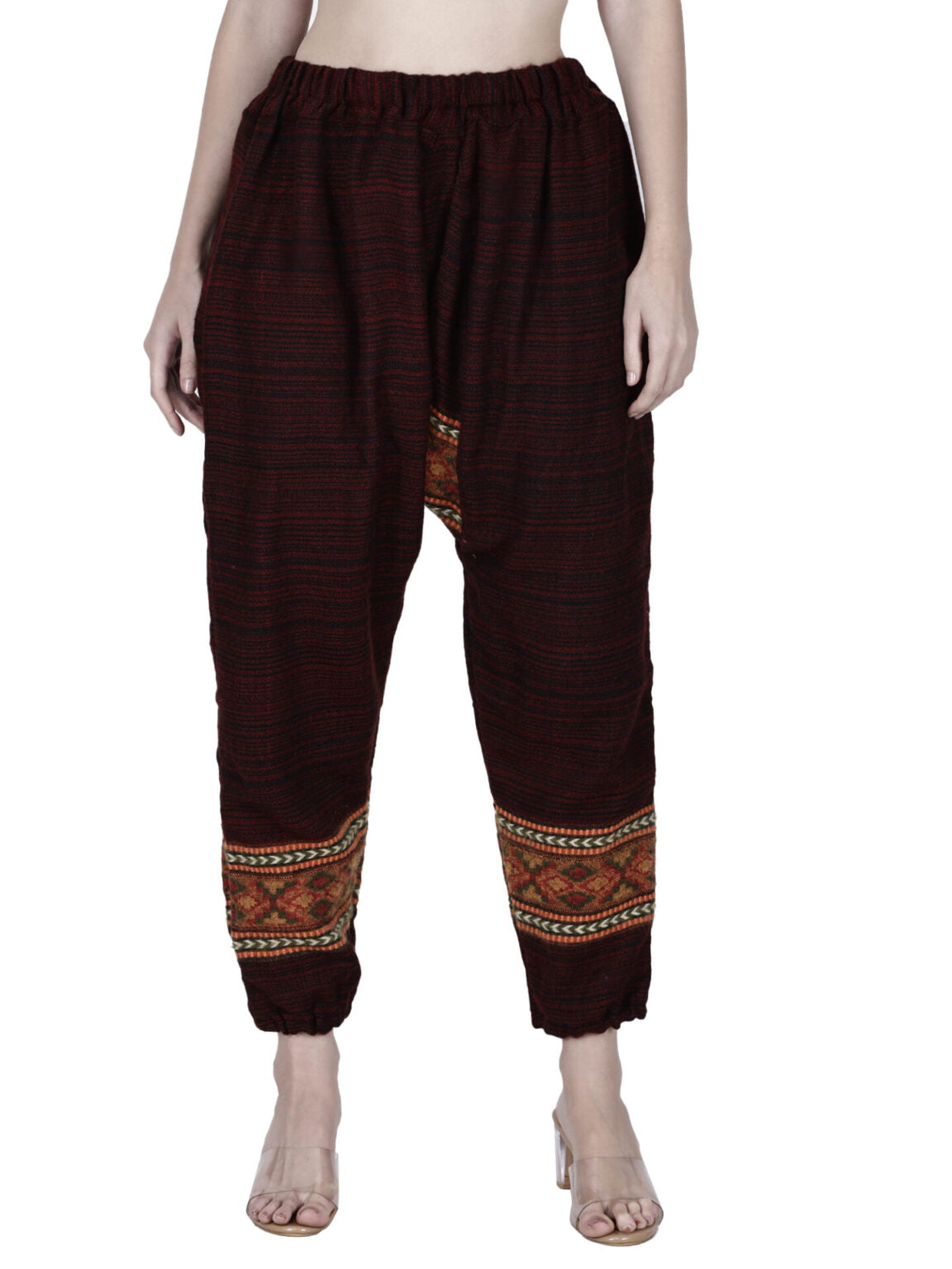 A person wearing aruna kullu handloom loose yoga pajama maroon singal patti, featuring an elastic waist and cuffs, intricate multicolored ankle pattern, and paired with open-toe heels. The upper body is not fully visible.