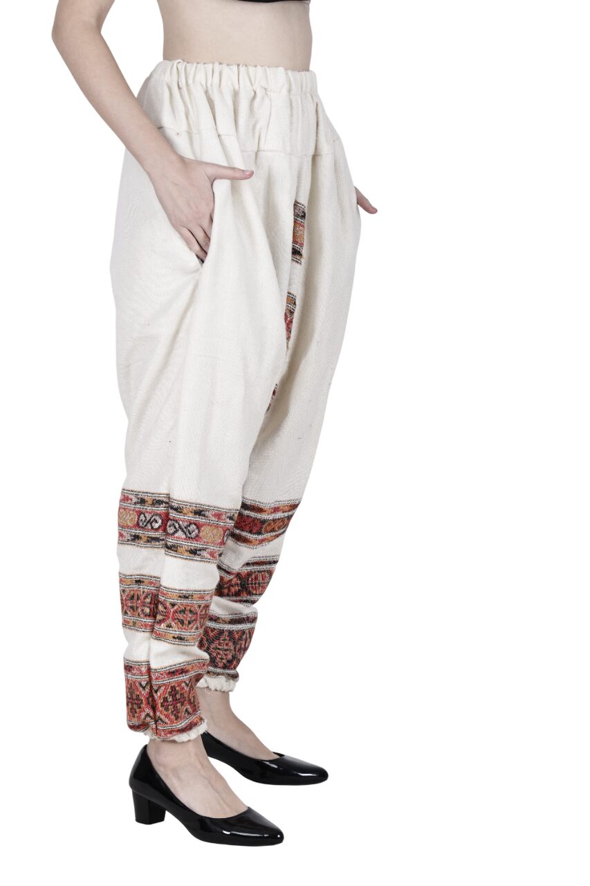 A person wearing high-waisted, loose yoga pant white 3 patti from aruna kullu handloom, featuring colorful embroidery near the ankles and paired with black patent heels. Photo shows only the lower torso and legs from the side.