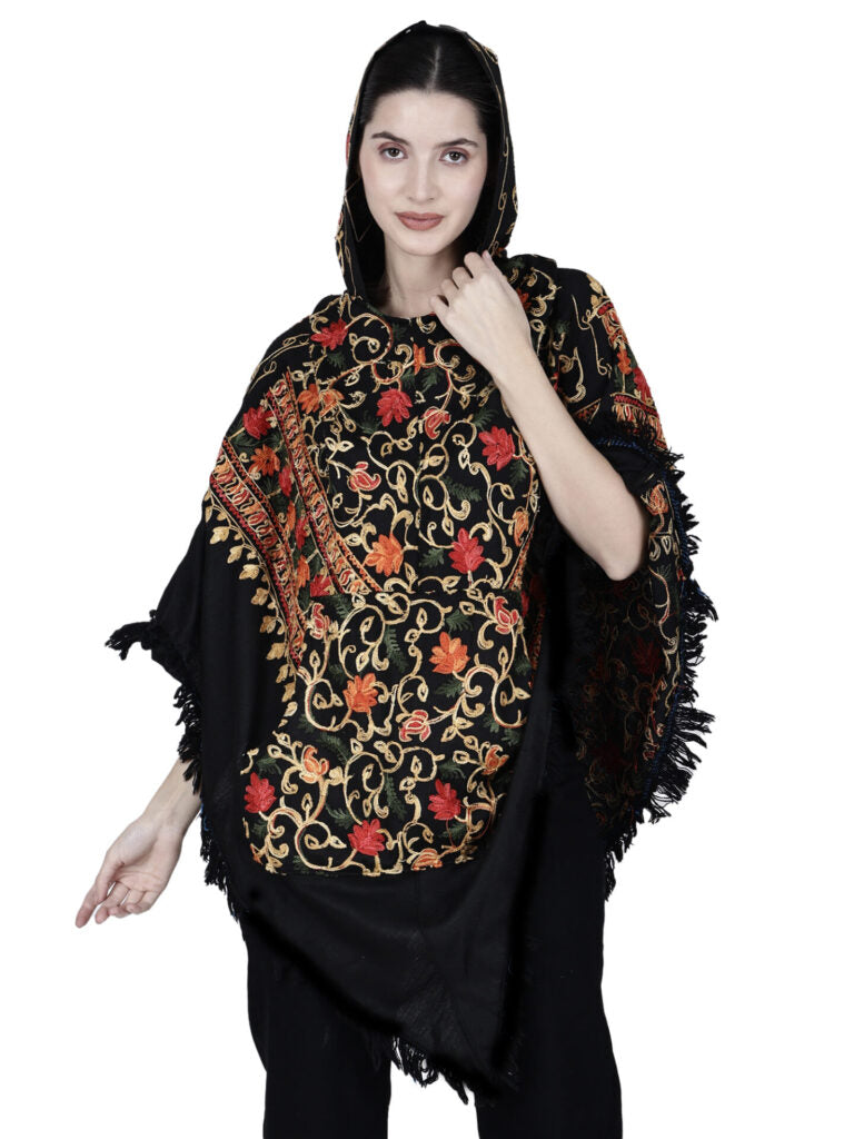 A woman models the aruna kullu handloom Kashmiri embroidered woolen poncho with hood for ladies in black, featuring red, orange, and gold floral embroidery and elegant fringe detailing that highlights traditional craftsmanship.