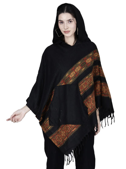 A woman wears the Aruna Kullu Handloom black woolen shawl poncho for girls (long 3 patti) by aruna kullu handloom, featuring red and gold stripes, fringed edges, a front pocket, and a modern-traditional design against a white background.