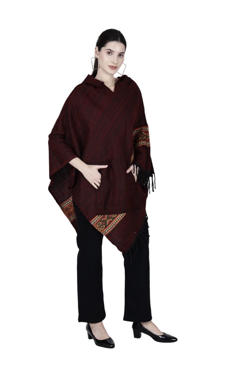 A woman stands against a white background wearing the aruna kullu handloom Poncho Top kullu shawl woolen poncho manroon singal patti, paired with black pants and heels, her hair tied back and one hand in her pocket.
