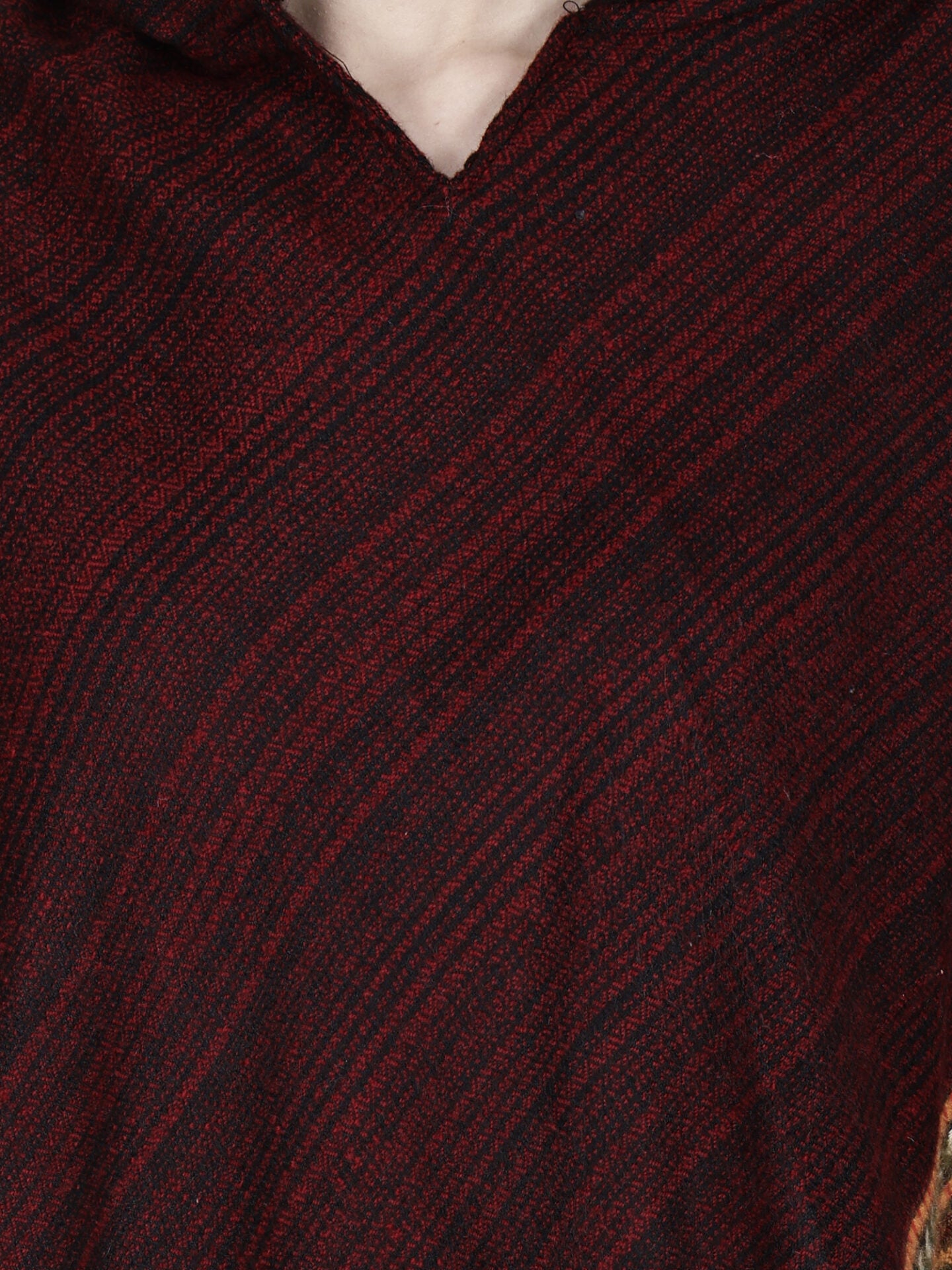 Close-up of the aruna kullu handloom kullu shawl woolen poncho with hood in maroon, featuring textured wool, diagonal lines, and geometric patterns. Only part of this elegant party wear and a bit of the neck are visible.