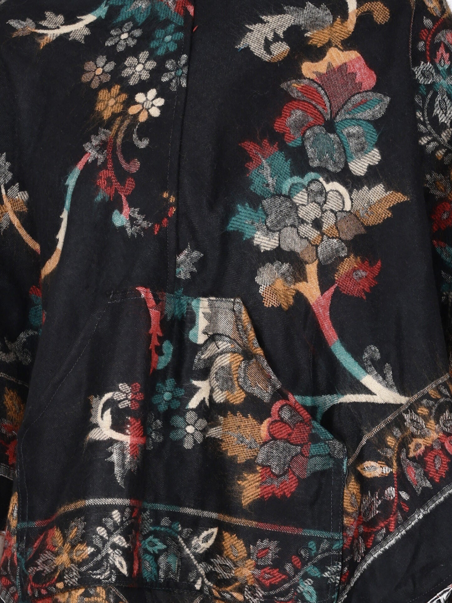 A close-up of the aruna kullu handloom Kashmiri black woolen poncho for ladies, featuring a hood and a central pocket, with a colorful floral pattern in red, teal, gold, and white—showing flowers, leaves, and branches.